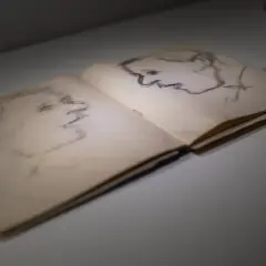 Szkice portretowe w otwartym szkicowniku. Po prawej stronie profil mężczyzny, po lewej ledwo widoczny zarys twarzy. Dzieło Artura Nachta Samborskiego.