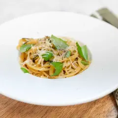 En portion spaghetti alla nerano, krämig och toppad med färsk basilika och riven ost.