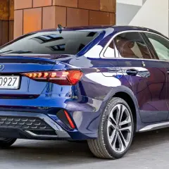 Błękitne, nowe Audi A3 sedan z polskimi tablicami rejestracyjnymi PY 90927, zaparkowane przed nowoczesnym budynkiem.