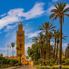 Torre Koutoubia, un lugar que ver en Marrakech, rodeada de palmeras y bajo un cielo azul con nubes.