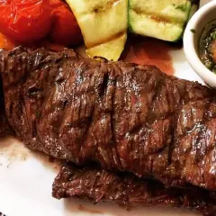 Jugosa entraña de vaca a la parrilla, acompañada de verduras asadas y una salsa chimichurri.