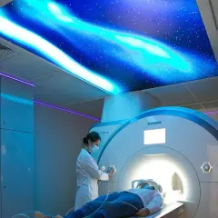 Pacjent leży w aparacie rezonansu magnetycznego, a technik przygotowuje badanie. Sufit ozdobiony jest motywem kosmicznym.