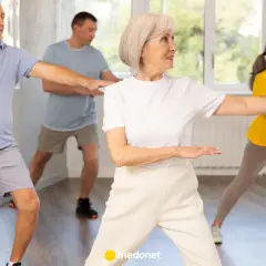 Seniorzy ćwiczą tai chi na krześle, synchronizując ruchy ramion.