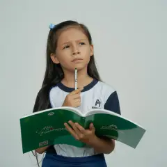 Bambina pensierosa con libro aperto, cerca la risposta a indovinelli per bambini.