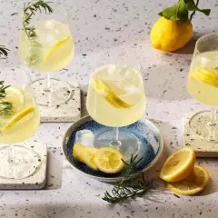 Quattro bicchieri di rinfrescante limoncello spritz, guarniti con limone e rosmarino, su un tavolo luminoso.