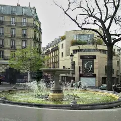 Fontanna na placu Pigalle w Paryżu, otoczona kamienicami i drzewami.