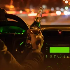 Kierowca trzyma butelkę piwa za kierownicą w nocy. W Niemczech obowiązuje ścisły limit alkoholu dla kierowców.