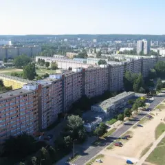 Długi, pomarańczowo-szary blok mieszkalny, znany jako najdłuższy blok w Polsce, rozciąga się wzdłuż ulicy. W tle widać inne budynki i zieleń.