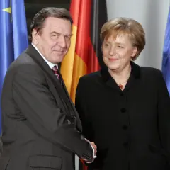 Gerhard Schröder und Angela Merkel, die erste Bundeskanzlerin Deutschlands, vor Flaggen.