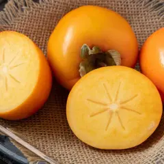Una varietà di cachi maturi, alcuni interi e altri tagliati a metà, rivelano la loro polpa arancione brillante e la forma a stella al centro.