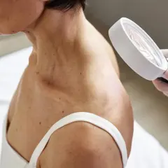 Dermatolog ogląda skórę szyi i ramienia pacjentki przez lupę.