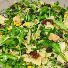 Pyszna sałatka z makaronem farfalle, rukolą, kurczakiem, kukurydzą i aromatycznymi suszonymi pomidorami. Posypana pestkami dyni i słonecznika.