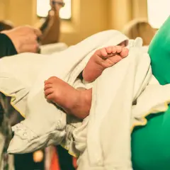 Les petits pieds d'un bébé, enveloppés dans un linge blanc orné, lors d'un baptême catholique.