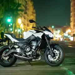 Kawasaki z650 cv blanca y negra, aparcada en una calle urbana de noche, con luces de edificios y semáforos de fondo.