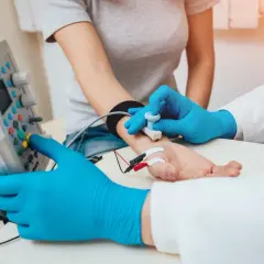 Lekarz w niebieskich rękawiczkach wykonuje próbę tężyczkową, przykładając elektrodę do przedramienia pacjentki.