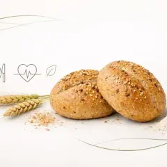 Dwie bułki grahamki posypane sezamem i siemieniem lnianym, obok kłosy zboża i garść mąki. Symbolika zdrowego żywienia.