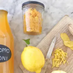 Bottiglia di sciroppo di limoni, limoni freschi, scorze e un coltello su tagliere. La sciroppo di limone ricetta della nonna è pronta!