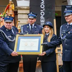 Uroczystość wręczenia nagród. Strażacy OSP w mundurach, z medalami, odbierają dyplom. Widać, jak nosić medale na mundurze OSP.