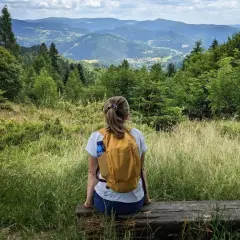 Kobieta z plecakiem odpoczywa na ławce, podziwiając malowniczy krajobraz górski. Idealne miejsce na wędrówkę po piwniczna zdrój szlaki.