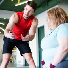 Trener w czerwonej koszulce pokazuje stoper osobie z nadwagą w jasnoniebieskiej koszulce.