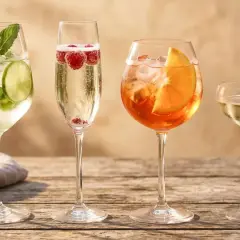 Cztery drinki na drewnianym stole: jeden z limonką i miętą, drugi z malinami, trzeci z pomarańczą, a czwarty z jeżyną. Idealne na letnie popołudnie, w tym orzeźwiający prosecco drink.