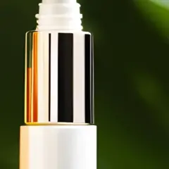 Zwei Pipettenflaschen mit goldenen Kappen, eine mit orangefarbener Flüssigkeit, die an Retinol und Vitamin C erinnert, vor einem grünen Hintergrund.