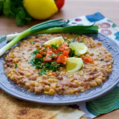 En tallrik med en mustig foul-rätt, toppad med tomat, persilja och citron. Ett utsökt recept för en smakrik måltid.