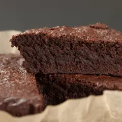 Wilgotne brownie bez jajek, posypane cukrem pudrem, ułożone na papierze do pieczenia.