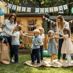 Radosne gry i zabawy dla dzieci klas 1-3 na przyjęciu urodzinowym w ogrodzie. Dzieci tańczą w kółku z opiekunkami, balony i girlandy tworzą świąteczną atmosferę.