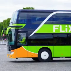Zielony autokar FlixBus jedzie ulicą. Kierowca w żółtej kurtce prowadzi pojazd. Czy FlixBus robi postoje? Tak, ten autokar na pewno zatrzymuje się na trasie.