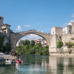 Mostar, Bośnia i Hercegowina: Słynny Stary Most z kamienia, tłumy ludzi na moście i brzegu, łodzie na rzece Neretwie.