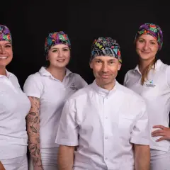 Zespół stomatologiczny w kolorowych czepkach i białych uniformach na czarnym tle.