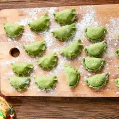 Zielone pierogi ze szpinakiem ułożone na desce, posypane mąką. Gotowe do gotowania, pachnące domowym obiadem.