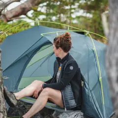 Kvinna vilar vid sitt tält, redo för camping i naturen.