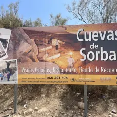 Cartel anunciando las Cuevas de Sorbas, con imágenes de exploradores y formaciones rocosas. Ofrecen visitas guiadas, restaurante y tienda.