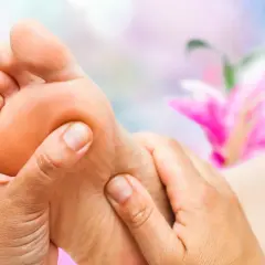 Close-up of hands massaging a foot with a blurred pink flower in the background.