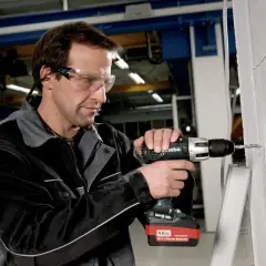 Un ouvrier utilise une perceuse sans fil Metabo, dont l'origine est allemande, pour percer un mur en parpaings.