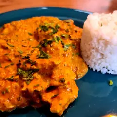 Ein Teller mit cremigem Hähnchen Tikka Masala, garniert mit frischer Petersilie, daneben ein Berg aus duftendem Reis.