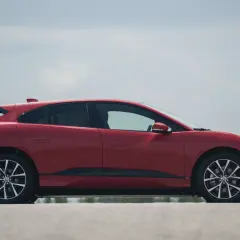 Czerwony jaguar elektryczny z profilu, z widocznymi felgami i linią dachu.