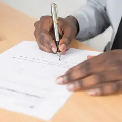 Main noire signant un document, peut-être une lettre de motivation pour un poste d'électrotechnicien.