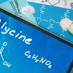 Tablet z napisem "Glycine" i wzorem chemicznym. Obok proszek w probówce. Dowiedz się, glicyna co to za związek.
