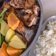 Sabrosa comida de Gambia: pollo asado, batatas, patatas y verduras verdes, acompañado de arroz blanco.