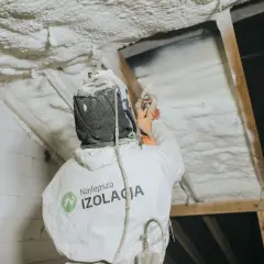Pracownik w kombinezonie natryskuje twardą piankę poliuretanową na poddasze, tworząc skuteczną izolację.