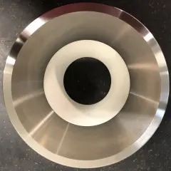 Componente metallico con finitura lucida, probabilmente acciaio inossidabile che contiene nichel, con un inserto bianco al centro.