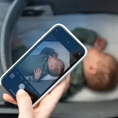 En hand håller en mobiltelefon och fotograferar en sovande bebis i en vagn. En billig babyvakt kan vara bra för att hålla koll.