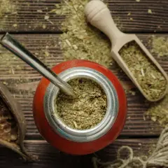 Czerwone naczynie z bombillą, drewniana łopatka z suszem i strąki – wszystko to sugeruje bogactwo yerba mate właściwości.