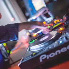 Les mains d'un DJ mixent sur une platine Pioneer, là où les DJs trouvent leur musique. Lumières colorées et ambiance festive.