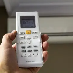 Mano sujetando control remoto de aire acondicionado, mostrando 16°C. La "A" en el aire acondicionado podría indicar modo automático o alguna función específica.