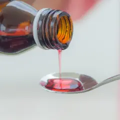 Czerwony syrop na kaszel mokry kapie z butelki na łyżeczkę.