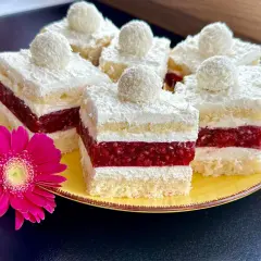 Pyszne ciasto rafaello z malinami, udekorowane wiórkami kokosowymi i malinową galaretką. Obok różowa gerbera.